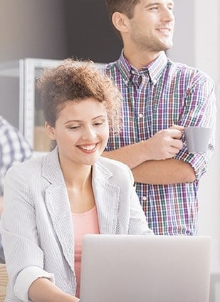 a girl smiling over laptop and a boy behind